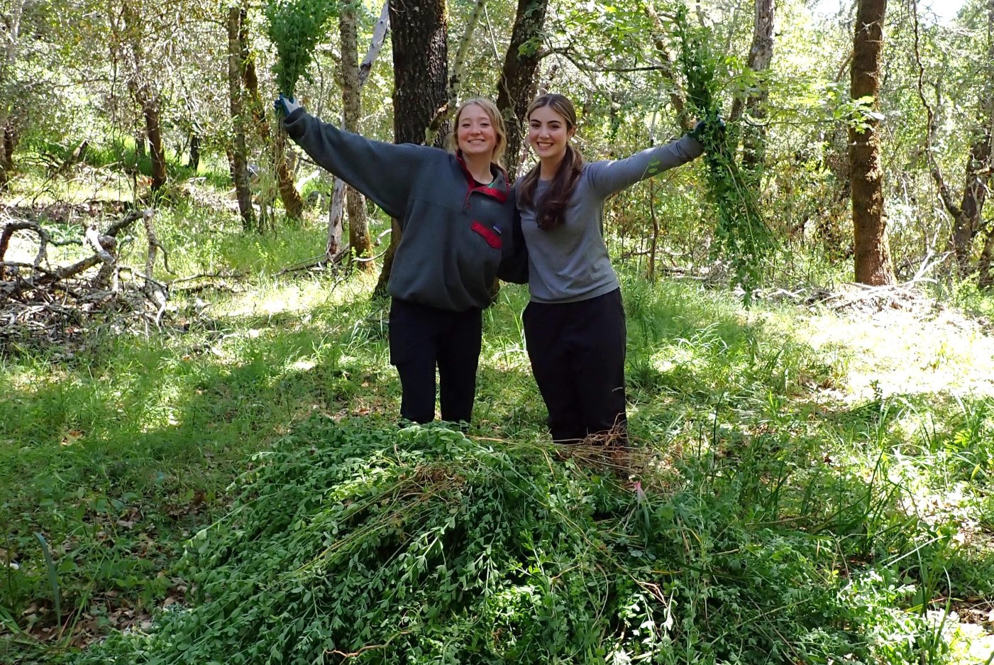 Two young women look over their pile of freshly-pulled weeds